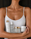 A woman in a white camisole holds four PROMISE skincare products against a dark wood background: face wash, toner mist, facial mask, and face cream.