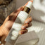 Hand holding a skincare bottle labeled 'Promises' with a blurred background